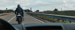 Image of a motorcyclist on road in from of a car
